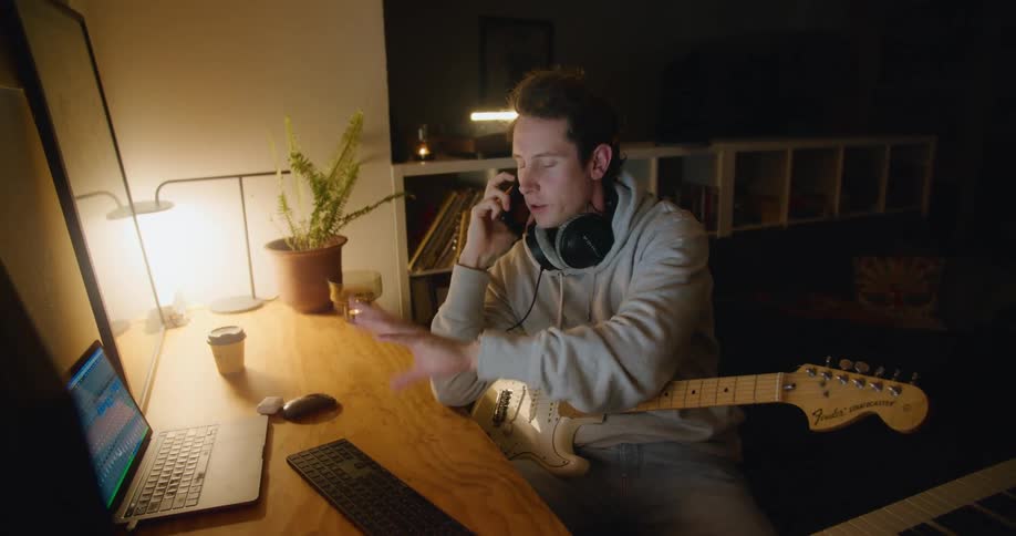 A man in a room with headphones using a laptop with a wall in the background