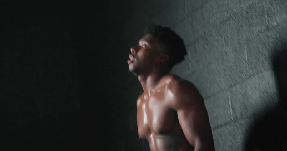 Muscular shirtless man gets up and walks in dark room breathing