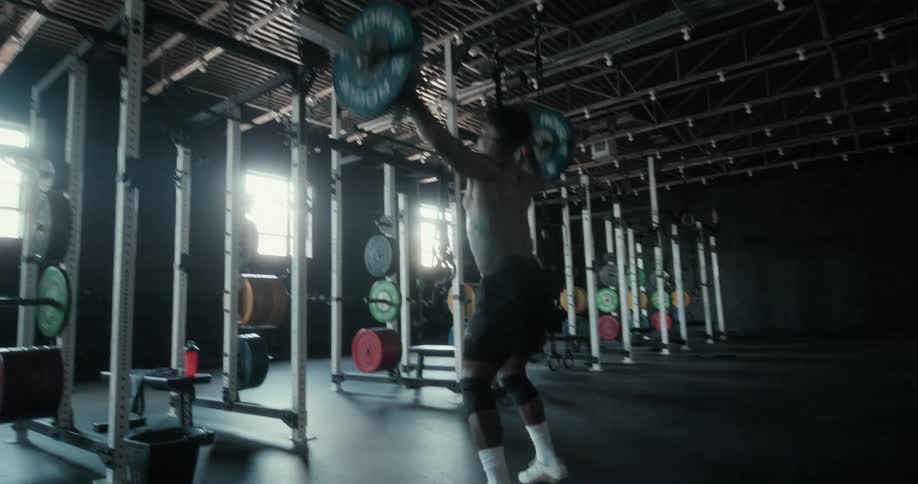Man lifts weight bar over his head in gym lit by sunlight from window