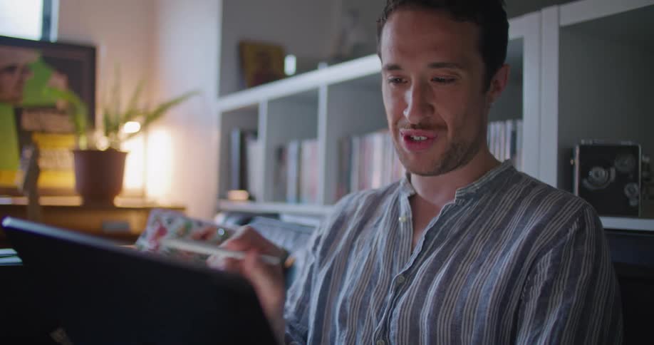 Man sits on couch gesturing and smiling while holding conversation over tablet video conferencing