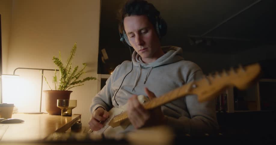 A man listens to some headphones then starts playing guitar