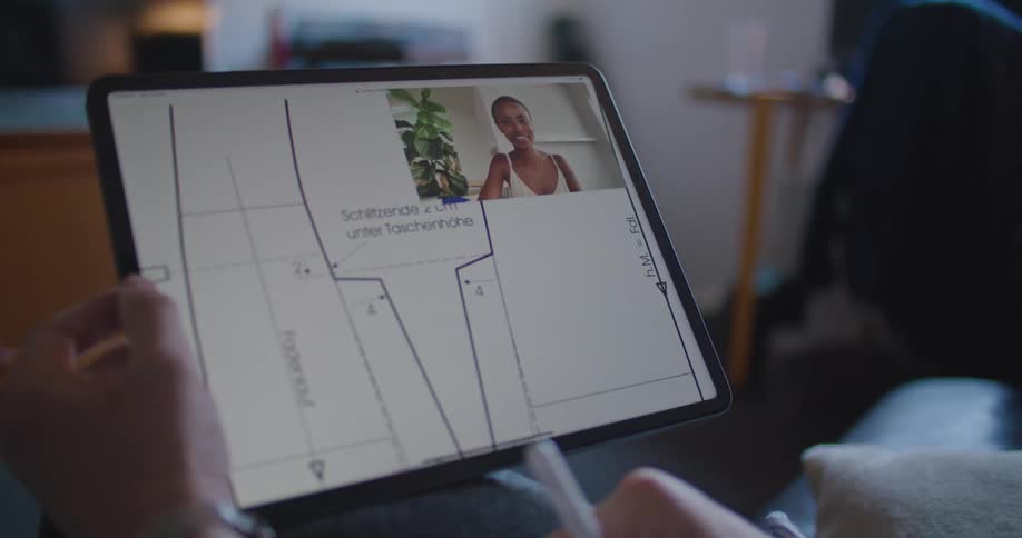 A man scrolls a pattern design on his tablet while a woman waves at him during a video call