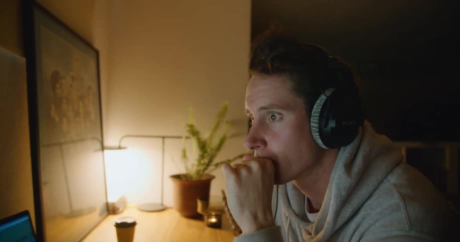 Man sits at table wearing headphones and adjusting digital control panel on laptop