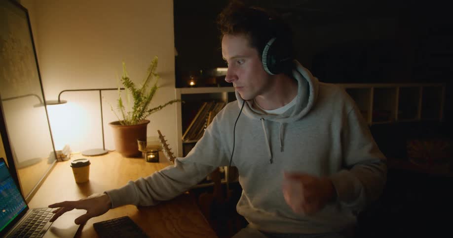 A man in a room with headphone sitting at a desk with a wall in the background