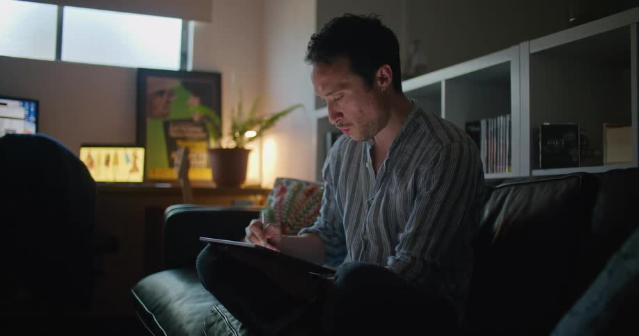 A man concentrates as he sits on his couch with his tablet computer