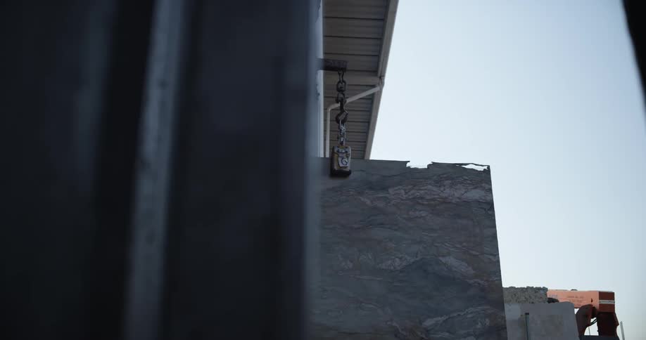 A slab of granite is slowly moved out of a warehouse door using a forklift jib attachment