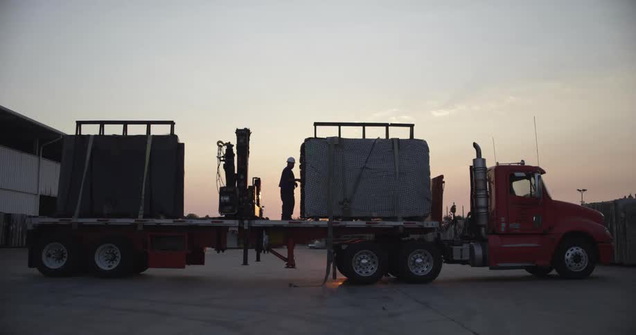 A person with a helmet on the back of a truck with the sky and clouds in the background