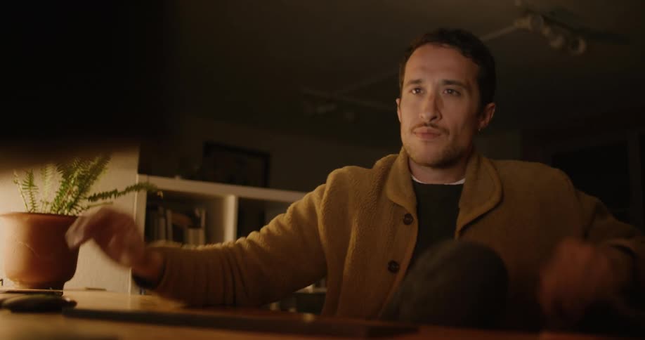 Man with brown coat black sweater and sock thinks and goes on to use desktop in room