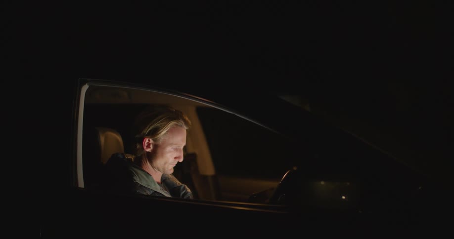 A man sitting in a car tapping on a tablet at night