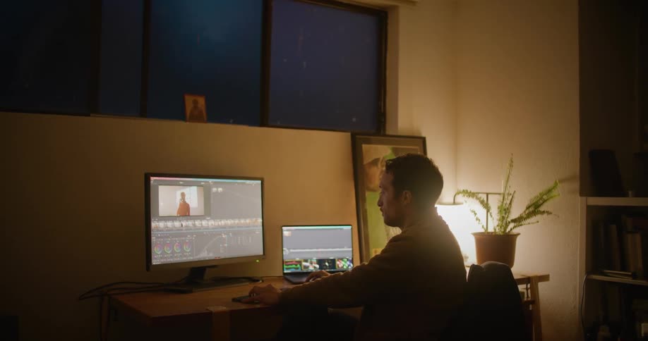 A man sits at his desk while working on his computer at night