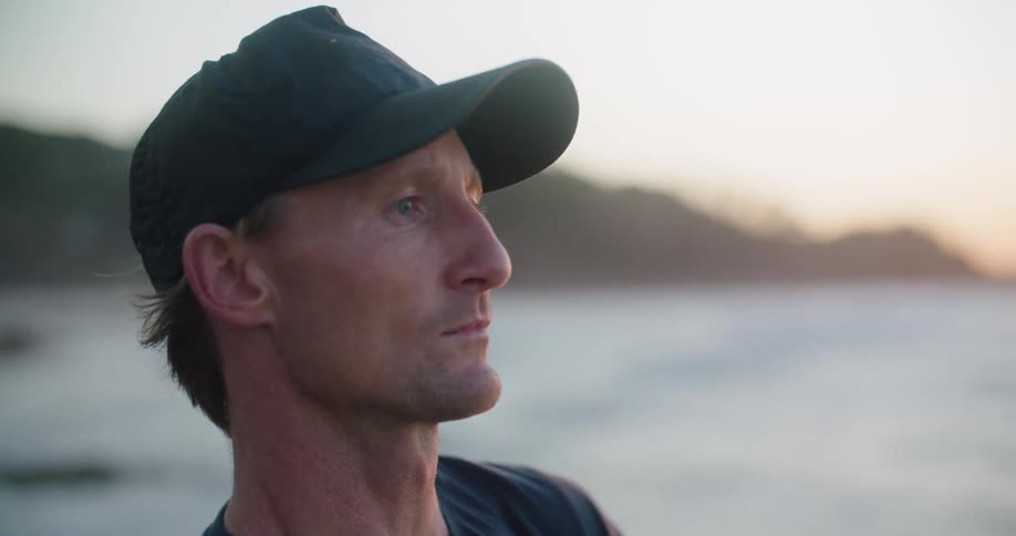 Man stand looking out as waves roll onto beach behind him