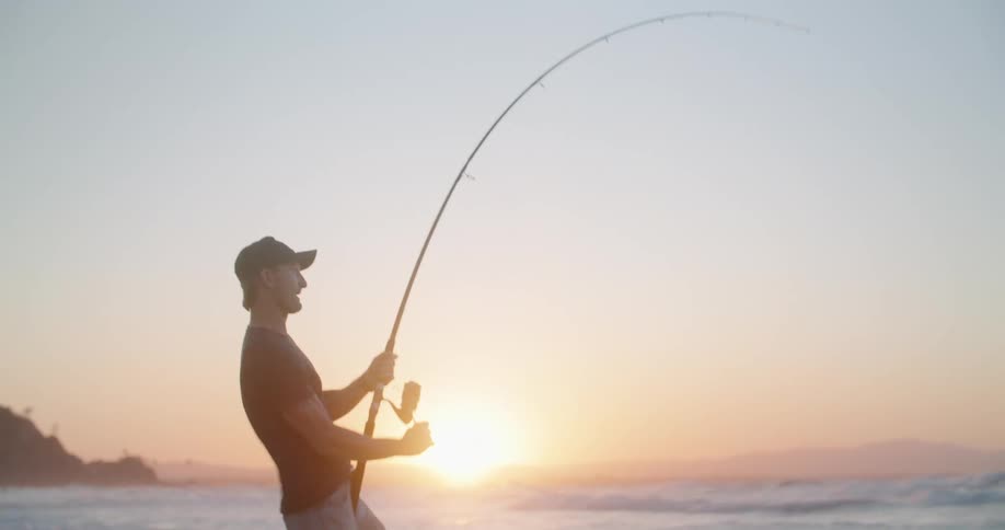 A man struggles to reel in his fishing rod while fishing along the coast