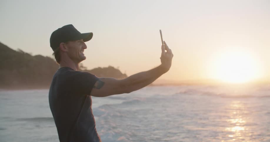 A man is talking with someone on his cellphone on the beach at sunrise