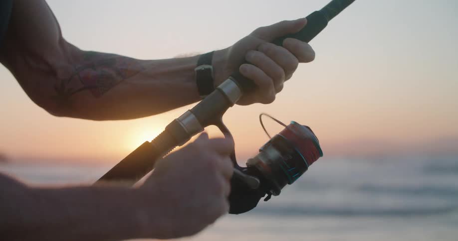 A man fishing on a beach at sunset