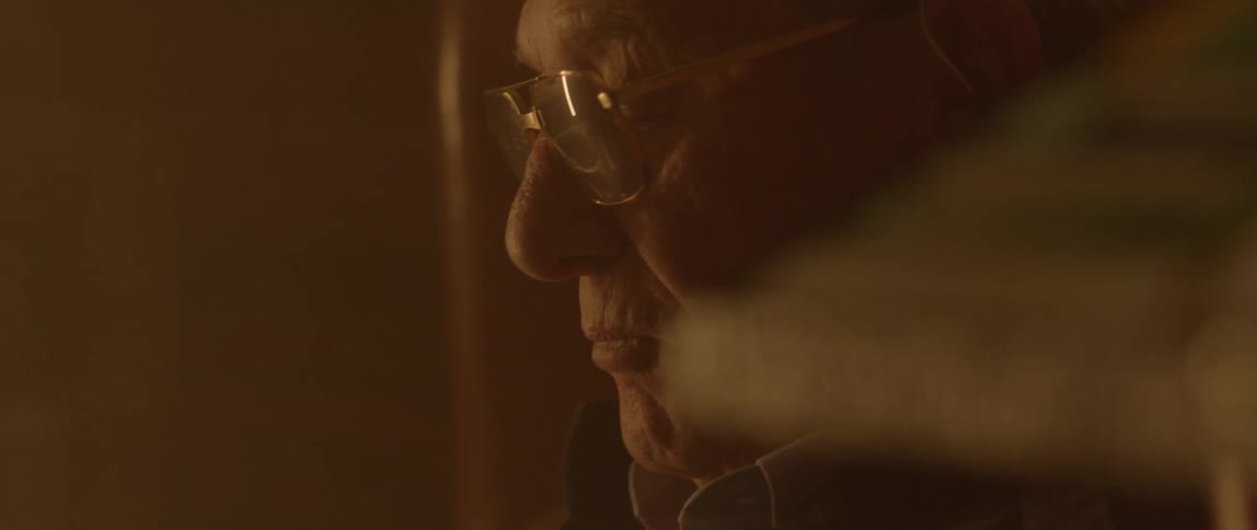 An elderly man sits in a chair near a burning fireplace