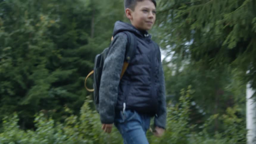 Boy carrying a backpack walking with his pet dog on a road near the pine trees