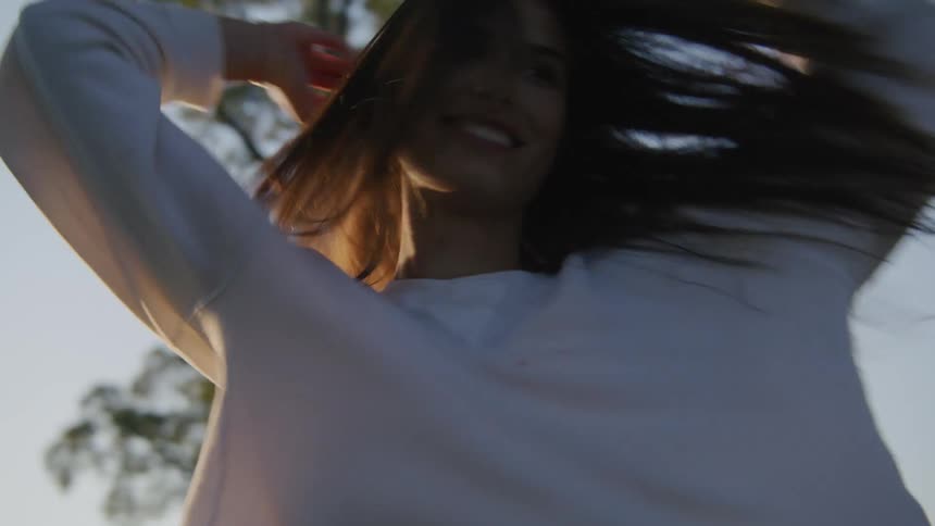 A woman laughs and smiles as she twirls causing her long hair to float around her