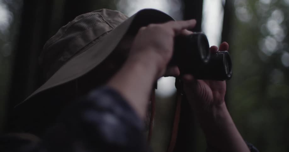 A man looks through binoculars while standing in the woods