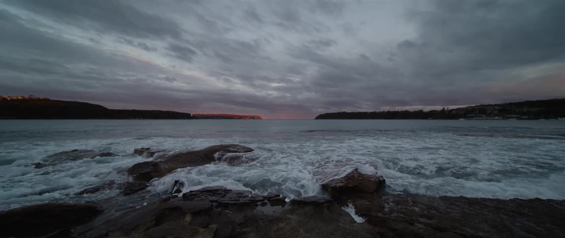 Waves crash onto a rocky beach under a cloudy sky
