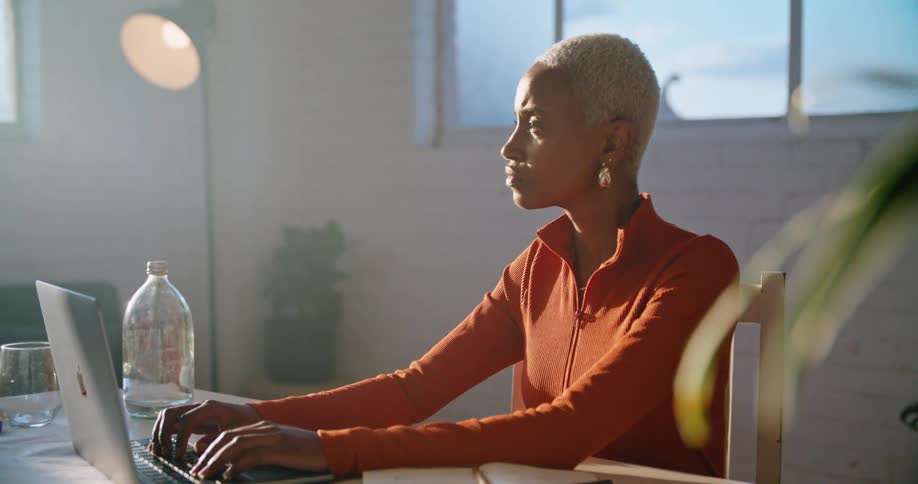 A young woman typing on a laptop pauses in thought for a moment before resuming her typing
