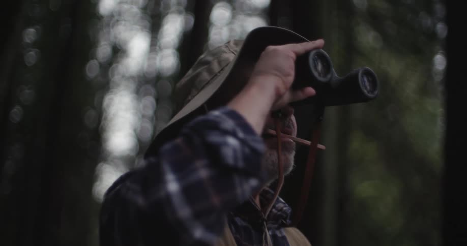 A man looks through binoculars and writes down what he sees while in the forest