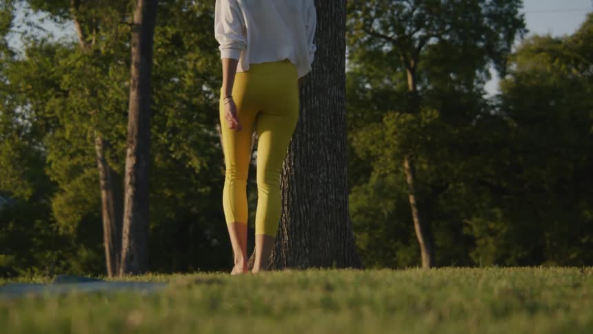 A woman walking barefoot on grass with trees the sky and clouds in the background