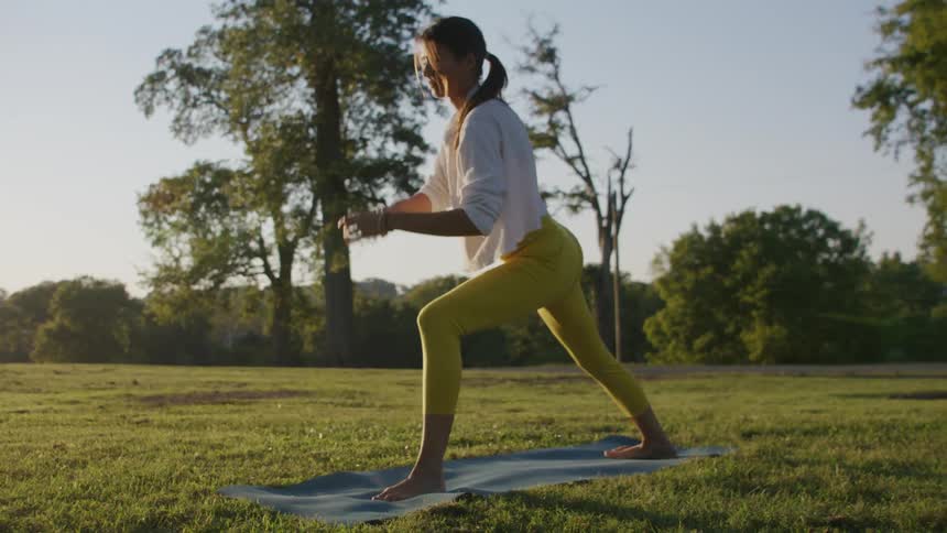 A woman stretching in a park with trees the sky and clouds in the background