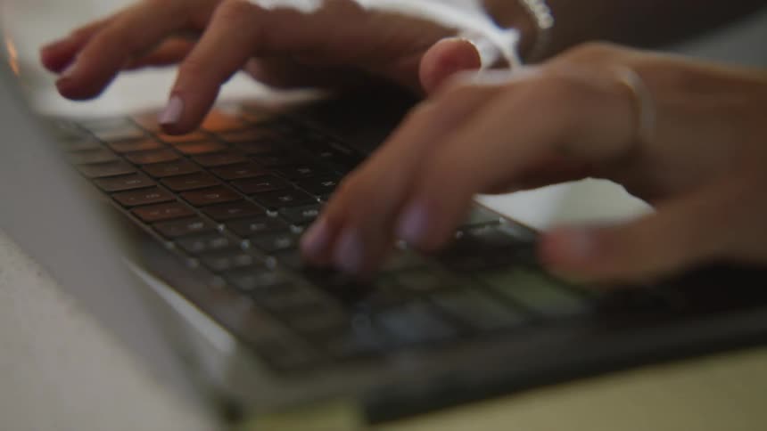 Woman typing on a laptop keyboard over a desk