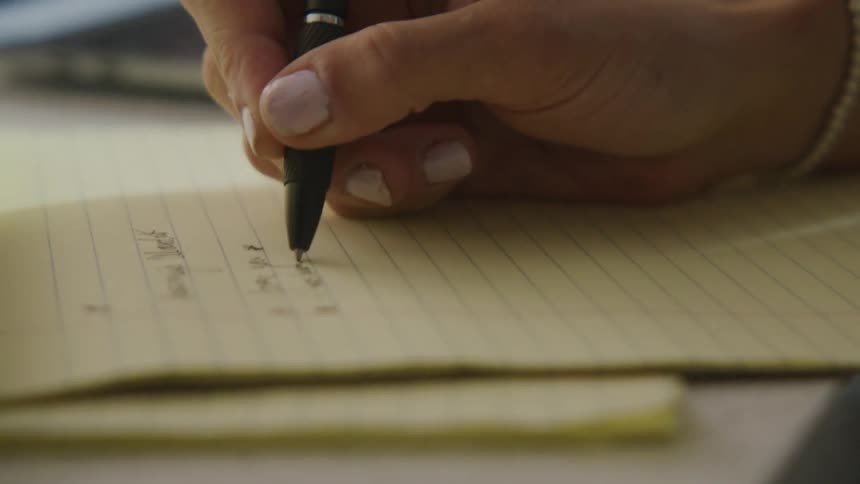 Woman writes on yellow notepad using black ink pen
