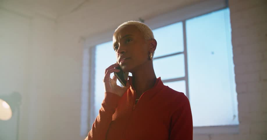 A young woman speaks on her smartphone while standing indoors during the day