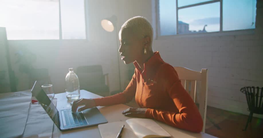 Woman sits at table holding conversation via video conferencing with bright sun shining through window