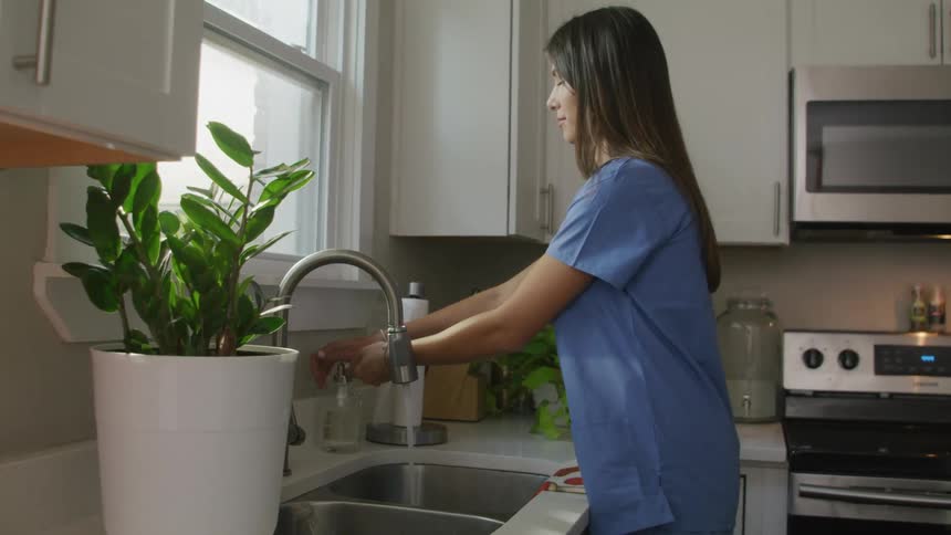 A woman walks to a sink in a kitchen and washes her hands