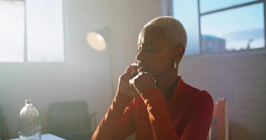 A woman is sitting down at a table with a computer in front of her and talking on the phone