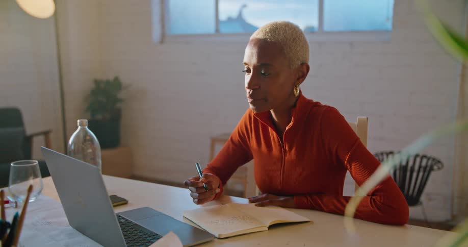 A woman is talking on her laptop and taking notes