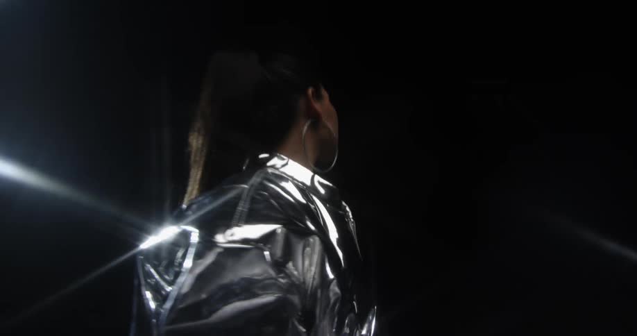 Woman stands on dark stage wearing reflective silver outfit