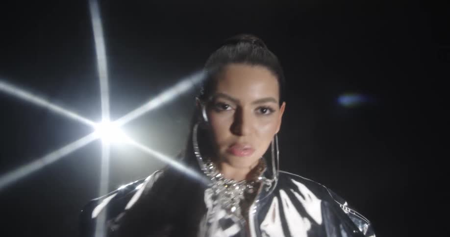 Woman poses in silver fashion outfit turning and walking on dark stage under spotlights
