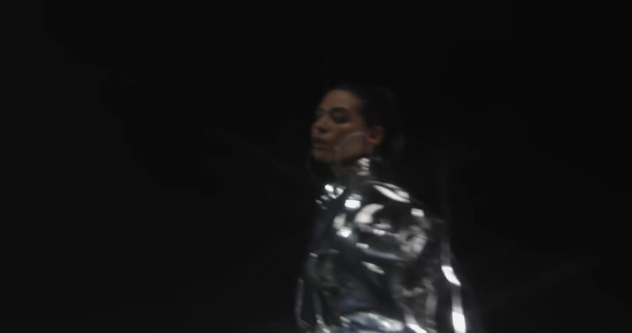 A woman wearing a silver outfit with earrings in a room with lights in the background
