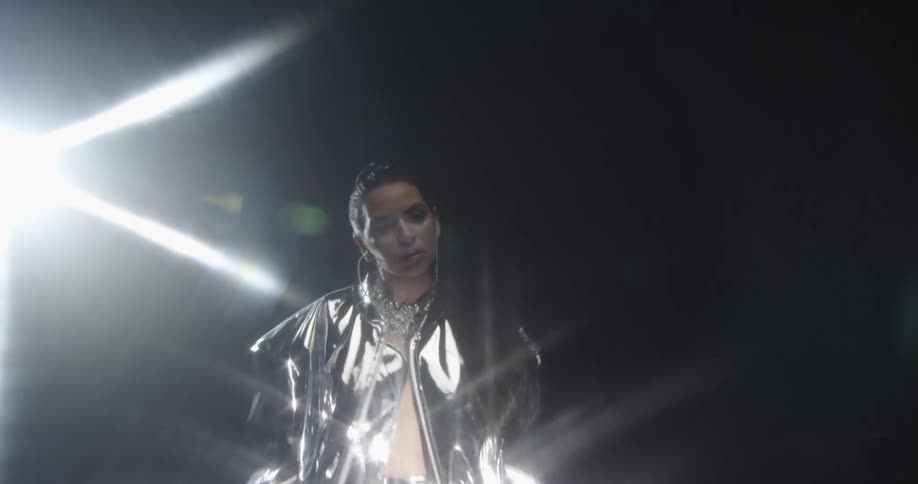 A bright light shines above a woman posing in a jacket made of silver reflective material