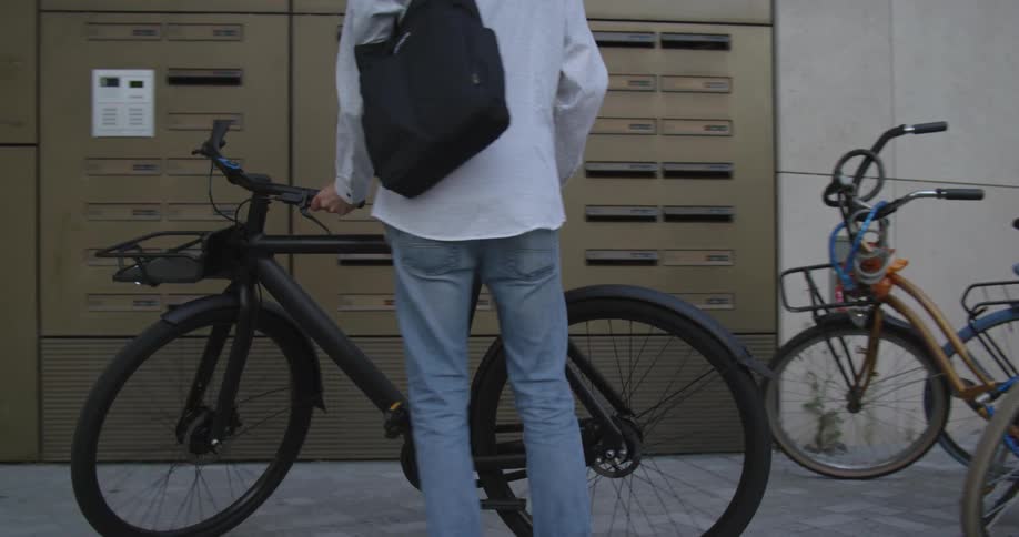 A man with a bag and glasses taking a bicycle from in front of a building