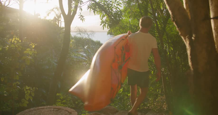 A man carries his kayak through the trees heading for the beach