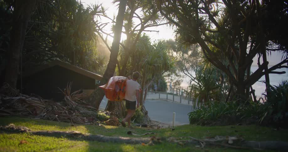 A man carries his surfboard from his yard to the ocean