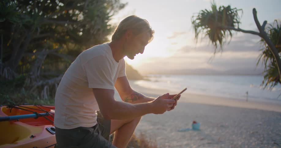 A man with a smart phone on a beach with the ocean and the sky in the background
