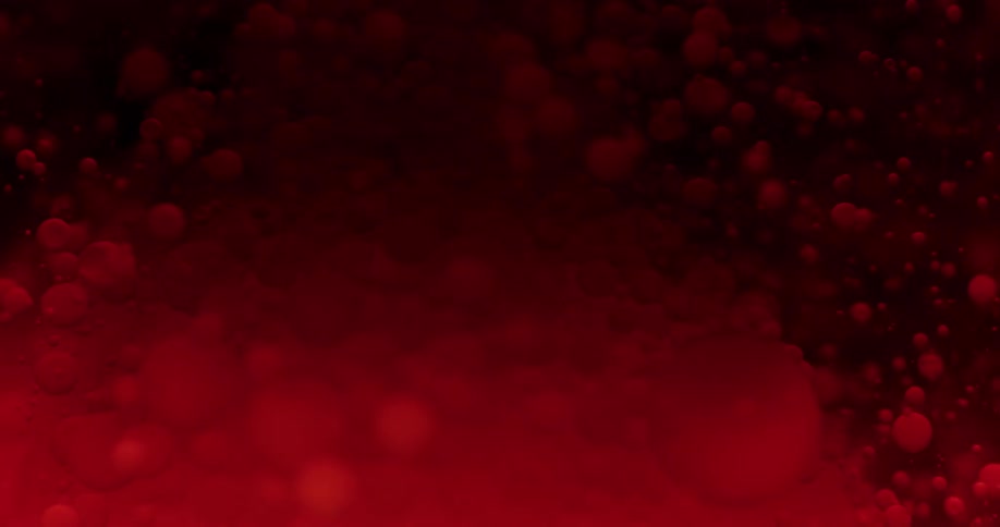 Dark red ink bubbles floating on liquid in front of black background