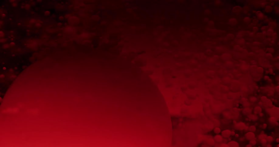 Dark red ink bubbles floating on liquid in front of black background