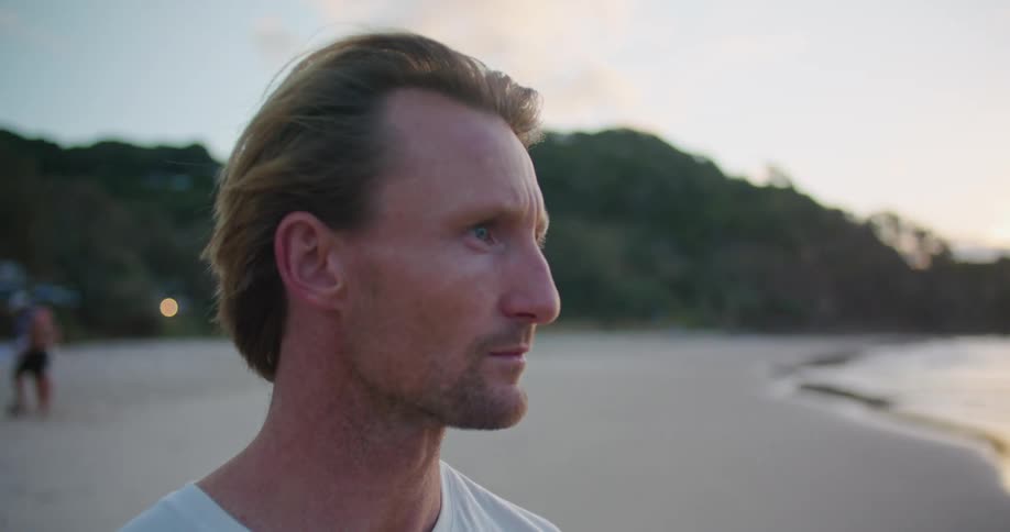 A man texting on a sandy beach at sunset