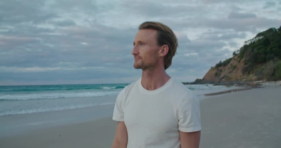 A man walks on the sand looking at the ocean waves