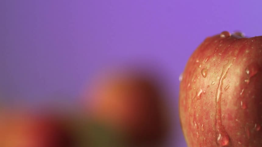 A drop of water falls onto an apple and runs down the side