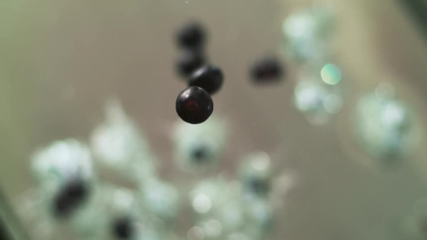 Black berries falling on a vat of clear water