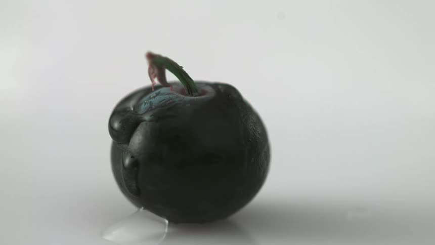 A piece of fruit is sitting on a table and a drop of water falls on it
