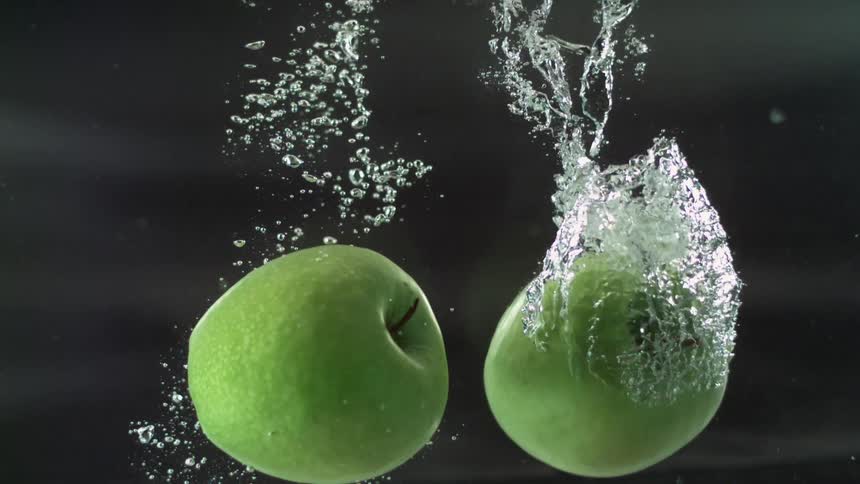 Two green apples sink in water before floating back up